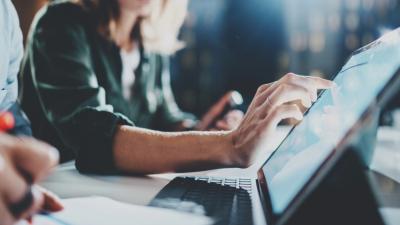 Hands typing on laptop keyboard in collaborative workspace, focus on detailed finger placement.